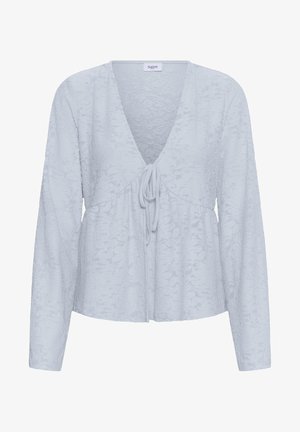 Blouse à manches longues bleu clair avec texture jacquard florale, col en V profond et fermeture à nouer sur le devant, étiquette "Saint" au niveau du col.