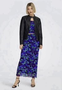 Jaqueta de couro preta sobre um vestido multicolorido com padrão floral em tons de roxo e verde, silhueta ajustada, e sapatos de tira no tornozelo.