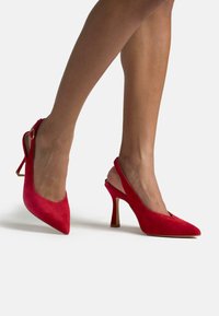 Rote Wildleder Slingback-Pumps mit spitzem Zehenbereich, schlankem Stiletto-Absatz und einem Knöchelriemen mit einem kleinen metallischen Akzent.