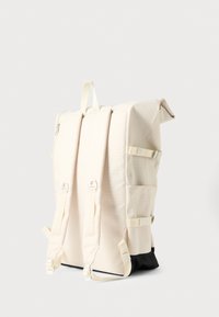 Bež ruksak od tkanine sa strukturiranim oblikom, podesivim naramenicama, srebrnim metalnim dijelovima i crnim dnom. Ima bočne džepove i gornju ručku.