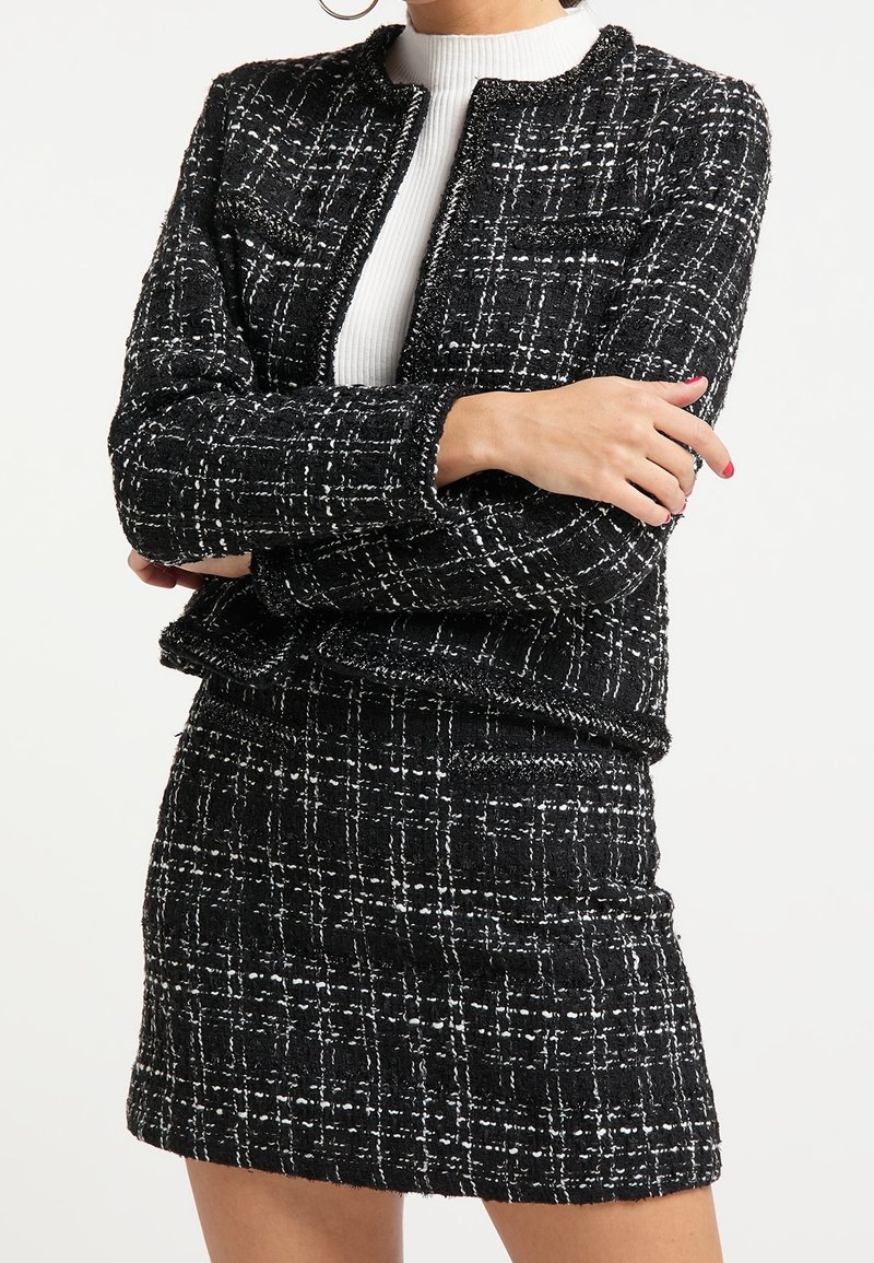 Czarna i biała tweedowa marynarka o dopasowanym kroju, z okrągłym dekoltem, bez zapięcia i teksturowanymi akcentami. W komplecie ze spódnicą w tym samym stylu.