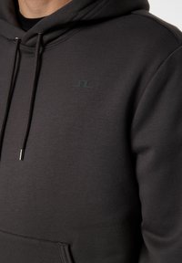 Mörkgrå hoodie av mjukt tyg, med en känguruficka, justerbar dragsko och logotypdetalj på bröstet.