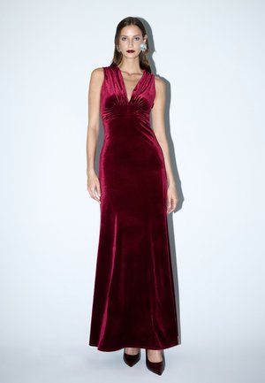 Bordeaux fluwelen avondjurk met een V-hals, geraffineerde lijfje en uitlopende zoom. Heeft een gladde textuur en een strakke silhouet.