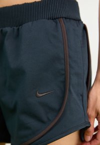 Dark blue athletic shorts made of soft fabric, featuring a brown accent trim and a small black Nike logo on the left side.