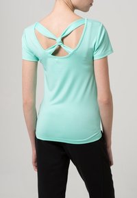 Miętowo zielony top z krótkim rękawem, o okrągłym dekolcie i unikalnym tylnym detalu związywanymi paskami oraz wycięciami.