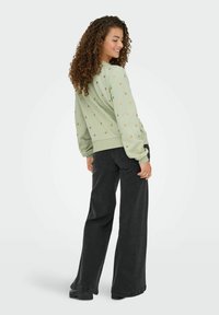 Sweatshirt vert clair avec motif de cœur, poignets et taille côtelés, associé à un jean noir taille haute à coupe large et des chaussures à plateforme noires.