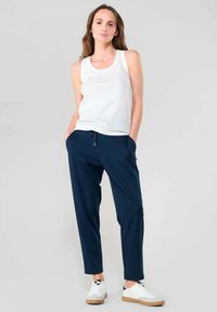 Witte tanktop, marineblauwe joggingbroek met taps toelopende pijpen, met trekkoord in de taille, gladde textuur, witte sneakers met beige zolen.