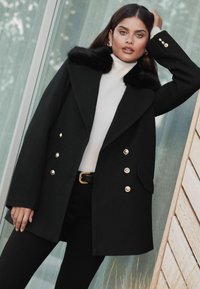 Čierny dvojradový kabát so zlatými gombíkmi a umelým kožúškom, s priliehavým strihom a bočnými vreckami. Vlnená textúra, moderný dizajn.