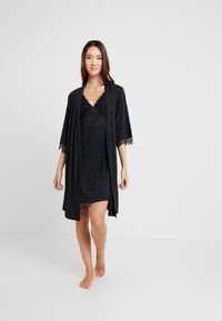 Svart nattlinne med spetskanter, lager på lager under en matchande lätt kappa med breda ärmar, vilket skapar en mjuk, elegant silhuett.