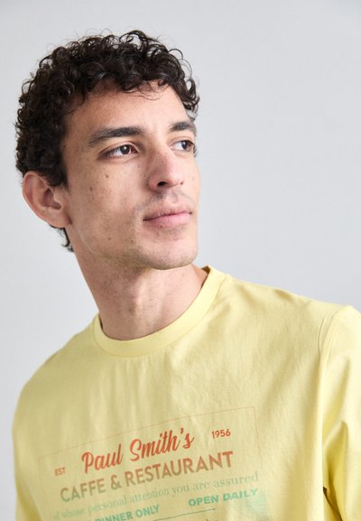 Yellow cotton t-shirt featuring a graphic design with "Paul Smith's Caffe & Restaurant" in red and green text, crew neckline, short sleeves.