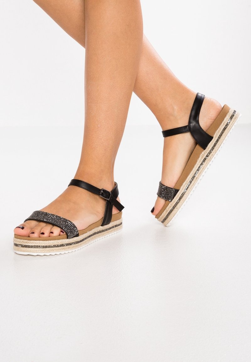 Sandales espadrilles noires avec une bride texturée ornée de strass, une semelle en wedge en jute, et une bride de cheville réglable.