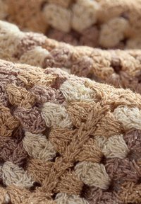 Coperta tessuta con texture che presenta gruppi alternati di filati crema, beige e marrone chiaro, con sottili fili metallici sparsi in tutto il tessuto.