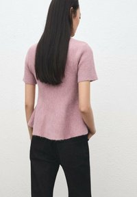 Haut en maille rose avec manches courtes et ourlet évasé. Le design présente une texture douce et est associé à un jean foncé. Esthétique subtile et minimaliste.