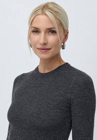 Tmavě šedý žebrovaný svetr s kulatým výstřihem a diskrétním logem. Hladká textura a přiléhavý střih zvýrazňují siluetu.