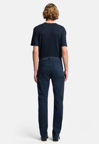 Dunkelblaue, gerade geschnittene Hose aus weichem Stoff, mit einem standardmäßigen Bund und subtilen Nähten. Kombiniert mit einem kurzärmligen Oberteil.