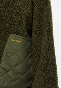 Oliiviroheline fliisjope tekstuurse pinnaga, millel on teemanttikujuline tasku. Taskul kuldseid kirjaga "Barbour" logo.