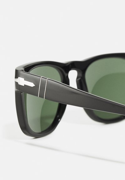 Black sunglasses with green lenses, featuring a prominent silver accent on the temples, rectangular frame, and glossy plastic finish.