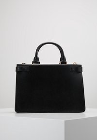 Borsa a mano nera in pelle con manici superiori, forma rettangolare e accessori in oro, posizionata su un piedistallo bianco su uno sfondo grigio chiaro.