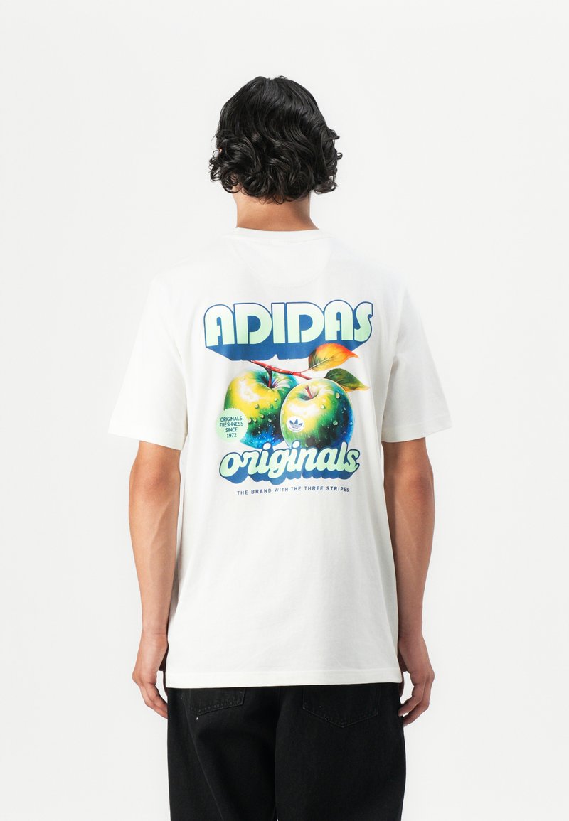 Fehér pamut póló, melyen egy nagy grafika látható két zöld almáról és a "ADIDAS originals" felirattal kék és zöld színben. Rövid ujjú, lazán illeszkedő fazon.