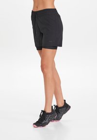 Mustat urheilushortsit, joissa on joustovyö ja nyöritys, sekä sileä rakenne. Yhdistetty mustiin ja vaaleanpuniin juoksukenkiin.