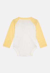 Langermet baby bodysuit med hvit kropp og lys gul raglanermer, laget av myk bomullsstoff, med rund hals.