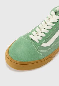 Grønn semsket sneakers med hvite lisser, gummisåle og kontrasterende sidestroker. Har sømdetaljer og et teksturert tåområde.
