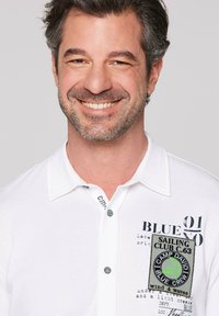 Polo bianco a manica corta, con tessuto testurizzato, patch ricamato verde e nero e bottoni a contrasto.
