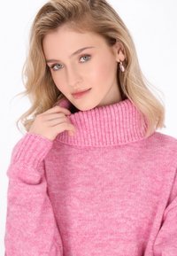 Rosa gestrickter Pullover mit hohem Rippkragen und langen Ärmeln, der eine weiche Textur und ein dezent meliertes Muster aufweist.