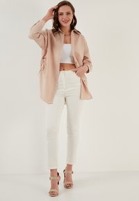 Svijetlo ružičasta prevelika košulja s dugmadi sprijeda, detaljem nabora sa strane, bijeli crop top, uske bijele hlače i bež sandale s petom.