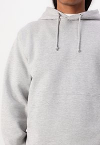 Ljusgrå munkjacka av mjukt tyg, med en framficka, snörning i huva och ribbade detaljer vid ärmar och nederkant.