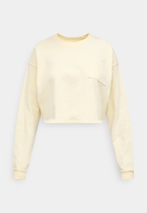 Izrezani pulover svijetlo žute boje, s dugim rukavima, rebrastim okruglim izrezom i džepom na prsima s detaljima šavova. Mekana tekstura tkanine.