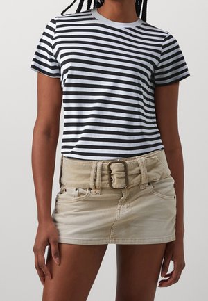 Frau trägt ein schwarz-weiß gestreiftes Kurzarmshirt mit horizontalen Streifen und einen beigefarbenen Cord-Minirock mit breitem Gürtel.