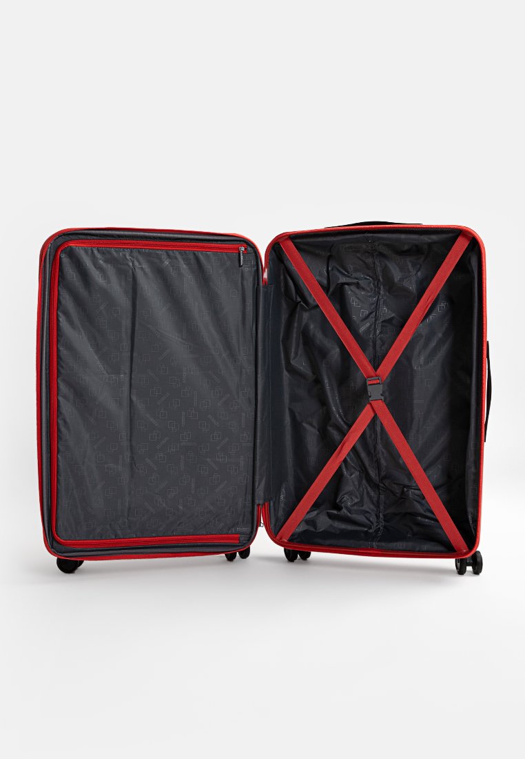 Valise rigide rouge avec intérieur noir, dotée d'une sangle en forme de X et d'un compartiment zippé. Roues lisses pour une mobilité facile.