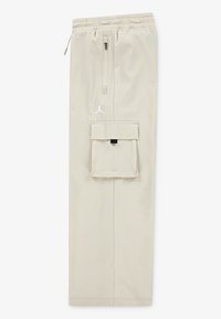 Beige cargo pants with an elastic waistband, a front zipper pocket, and a large patch pocket on the side. Features white Jumpman logo.