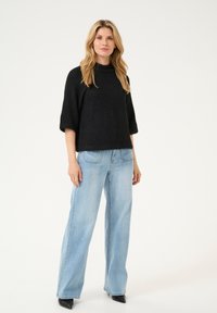 Schwarzer gestrickter Pullover mit hohem Kragen und Dreiviertelärmeln, kombiniert mit hellblauen weit geschnittenen Jeans und schwarzen spitzen Schuhen.