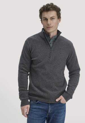 Dunkelgrauer Pullover aus strukturiertem Strickstoff, mit einem Reißverschlusskragen und gerippten Bündchen, kombiniert mit blauen Jeans.