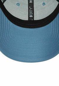 Gorra de béisbol azul con visera negra, que presenta una tela texturizada y una etiqueta de marca interior. Corona suave y acentos cosidos.