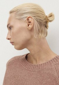 Light pink knitted sweater with a ribbed neckline, worn by a person with blonde hair styled in a low bun, side profile view, minimal background.