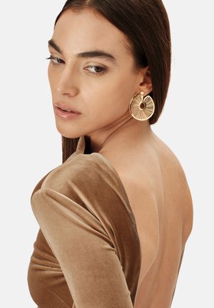 Top in velluto marrone a maniche lunghe con schiena scoperta, che mostra una texture liscia. Orecchini dorati a cerchio con motivi radiali e un foro centrale.