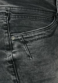 Vaqueros de mezclilla negros con un bolsillo frontal con remache de metal, costuras en contraste y una tela suave y ligeramente texturizada.