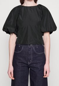 Top corto nero con maniche a sbuffo, realizzato in tessuto liscio; abbinato a pantaloni a vita alta in denim scuro a gamba larga con cuciture a contrasto.