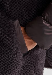 Strukturierter dunkelgrauer Stoff mit einer flauschigen, weichen Oberfläche, einem glatten, glänzenden schwarzen Kragen und einer sichtbaren Innentasche.