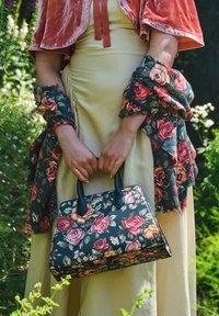 Tas met bloemenmotief en zwarte leren handvatten, met veelkleurige rozen ontwerpen op een donkere achtergrond, gecombineerd met een bloemenwikkel.