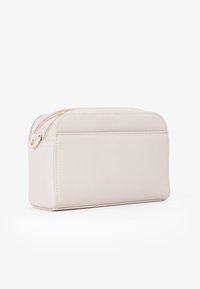 Borsa cosmetica sintetica beige di forma rettangolare, con chiusura a zip e tasca laterale. Presenta una texture liscia e dettagli hardware in tonalità oro.