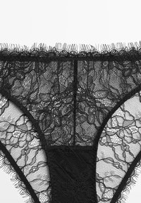 Black lace thong featuring floral patterns, fine mesh texture, and soft elastic trim, with a solid black panel at the back for coverage.