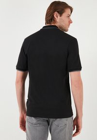 Černé polo tričko vyrobené z bavlny, s krátkými rukávy, má kontrastní barvu límce a lemů rukávů, hladkou texturu a přiléhavý střih.