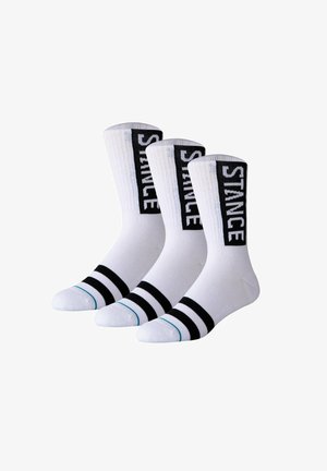 Drei weiße Crew-Socken mit zwei schwarzen Streifen in der Nähe der Zehen und "STANCE" vertikal auf schwarzen Bändern entlang der Wade geschrieben.