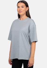 T-shirt en coton gris clair avec une coupe décontractée, manches courtes, col rond et texture lisse. Pas de motifs visibles ni de détails matériels.