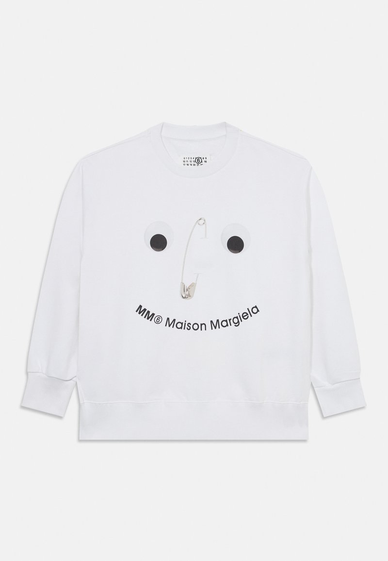 Balta sporta krekla ar lielu acu grafiku un drošības adatām, apakšā izdrukāts teksts "MM® Maison Margiela". Mīksta auduma.