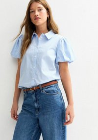 Light blue striped short-sleeve button-up shirt with a collar, paired with high-waisted blue jeans and a brown belt.